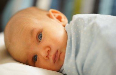 Evde bebek yatağında mavi battaniye içinde yatan hassas ciltli yeni doğmuş bir bebek. Yakın çekim fotoğrafı. Hassasiyet, aşk