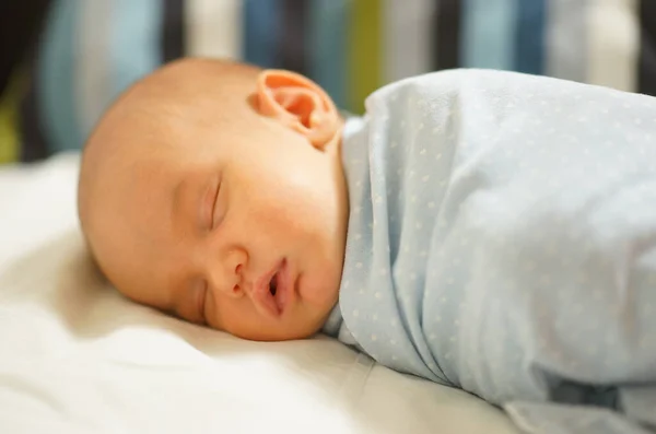 Newborn baby with sensitive skin sleeping sweet in blue blanket in baby bed at home. Closeup photo. Delicacy, love