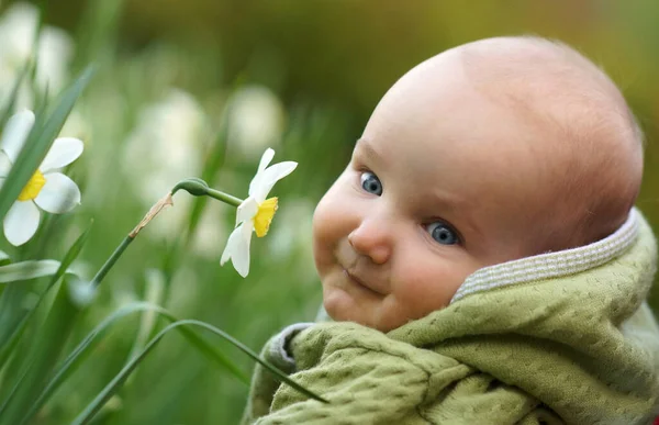 Портрет маленької милої усміхненої дитини в зеленому одязі біля біло-жовтих квітів нарцис, крупним планом, зовні в парку — стокове фото