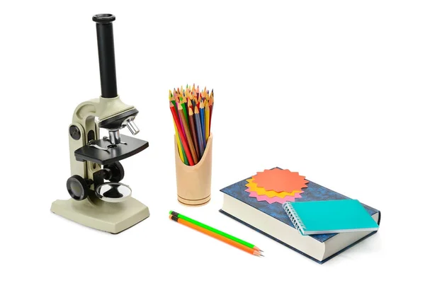 Microscopio, libro de texto y otros útiles escolares aislados en blanco — Foto de Stock