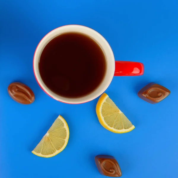 Červený hrnek s čajem, plátky citronu a čokoládové bonbony na modré — Stock fotografie