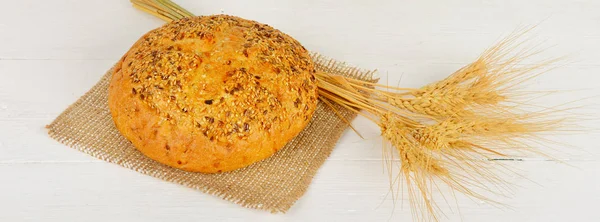 焼きたてのパンと木製のテーブルの上の小麦。ワイド写真. — ストック写真