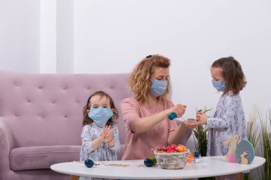 Anne ve kızları yumurta boyuyor. Mutlu aile Paskalya için hazırlanıyor. Annesi Coronavir 'e karşı kızının maskesini takıyor. Evde karantina.