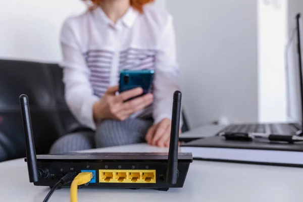 Wi-Fi yönlendiriciyle evdeki oturma odasında akıllı telefon kullanan kızıl saçlı bir kadının yakın çekimi.