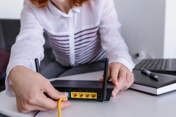 Redhead Woman connects the internet cable to the router\'s socket. Fast and wireless internet concept