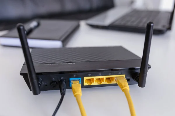 Wired modem router network, sitting on a white table, next to a laptop and an address book