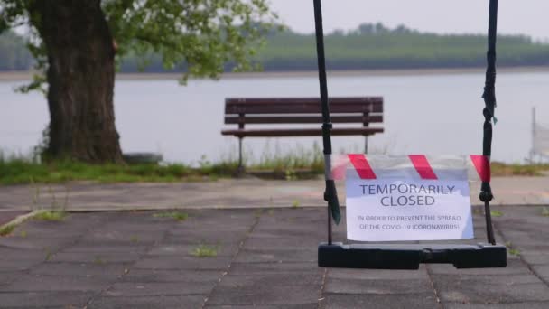 空荡荡的秋千 用红白相间的预防带防止考罗纳威病毒的传播 有长椅 世俗树和水湖背景 — 图库视频影像