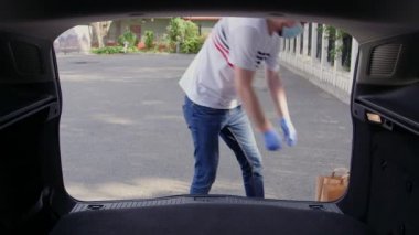 Maske takan kişi bir arabanın bagajına kutu ve kese kâğıdı koyar. Salgın bir koronavirüsün ortasında gönüllü bir iş.