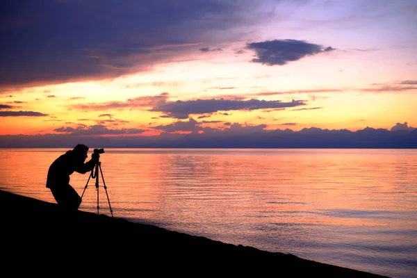 Fotograf vor dem Hintergrund des Sonnenuntergangs am Meer Stockbild