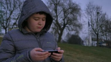 Genç çocuk smartphone kullanarak Gölü kıyısında ayakta. Kış öğleden sonra.