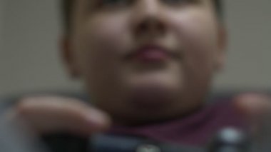 Oturma ve koltukta, rahatlatıcı ve bilgisayar oyunu oynamak genç çocuk. Holding ve oyun kumandasını kullanarak.
