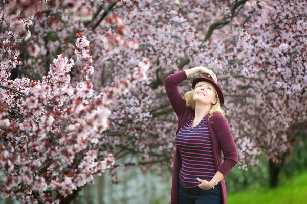 Çiçek açması tree yakınındaki mor fedora şapkalı uzun saçlı beyaz sarışın kadın