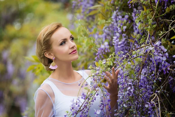 Mor wisteria yakın sarı saçlı genç bir Kafkas kadın portresi, yukarı bakıyor.