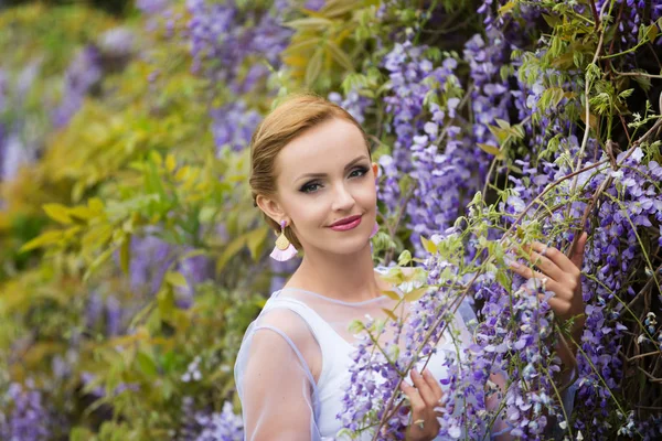 Mor wisteria yakın sarı saçlı genç bir Kafkas kadın portresi, kameraya doğru bakıyor.