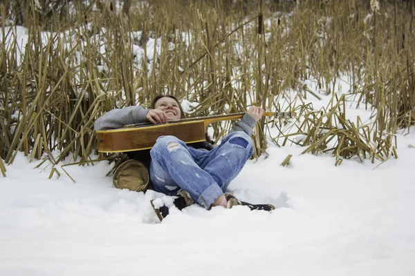 Bastante risueño chica tendida en la nieve y tocando la guitarra . —  Fotos de Stock