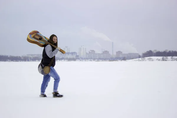 Chica bastante sonriente caminando sobre la nieve con la guitarra —  Fotos de Stock