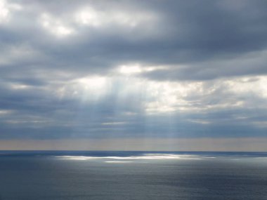 Deniz üzerinde bulutların arasından parlayan güneş ışığı.