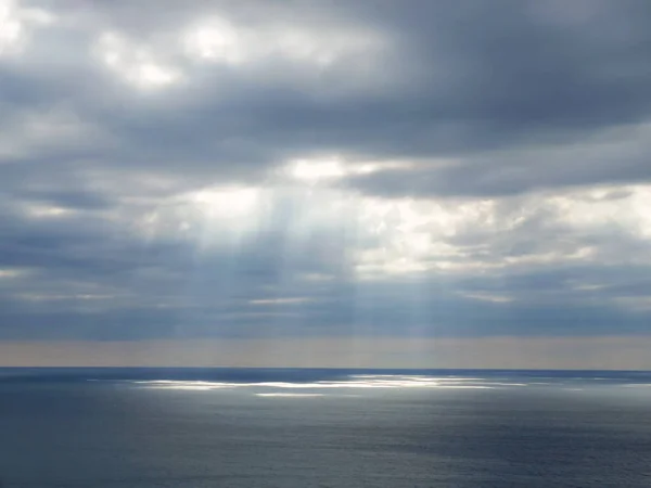 Το ηλιακό φως λάμπει μέσα από σύννεφα πάνω από τη θάλασσα. Φωτογραφία Αρχείου