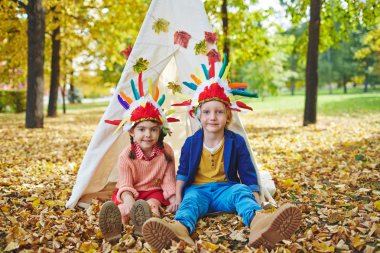 Two kids playing Indians in park clipart