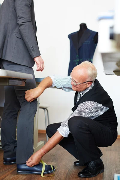 Tailor going to measure trousers of man — Stock Photo, Image