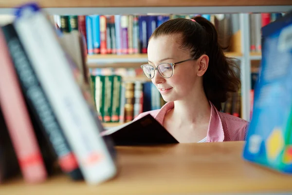 Tiener student lezen tussen boekenkasten — Stockfoto