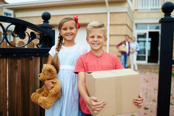 Siblings standing by fence of new house — Stock Photo, Image