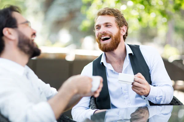 Дружелюбные мужчины с кофе разговаривают в кафе — стоковое фото