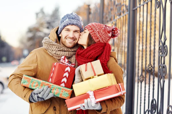 Szczęśliwa dziewczyna z giftboxes całując swojego chłopaka — Zdjęcie stockowe