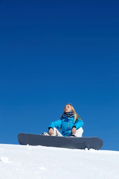 Kvinna sitter med snowboard på toppen av ett berg — Stockfoto