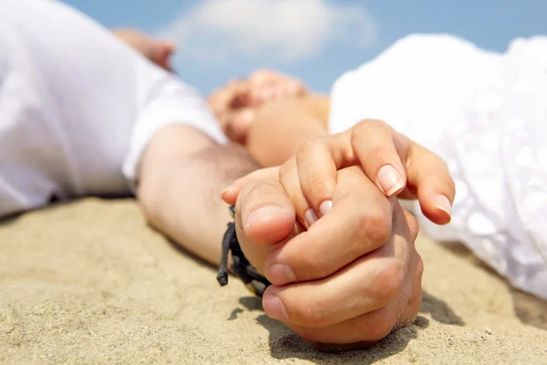 Hands of young couple lying on sand — Stock Photo, Image