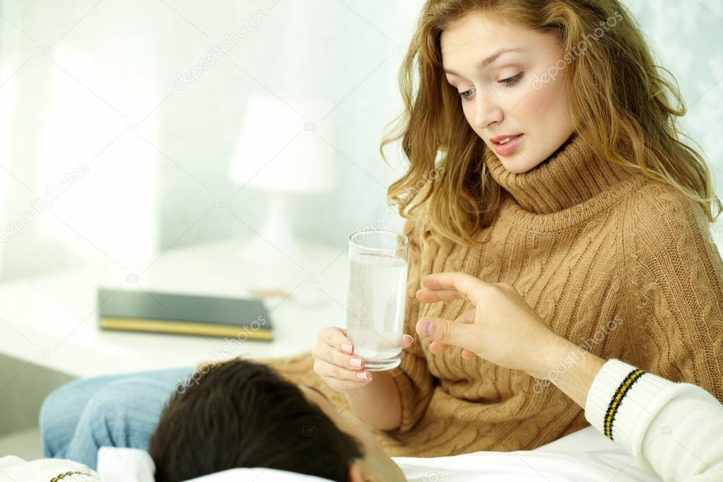 woman giving glass of water to her sick husband 
