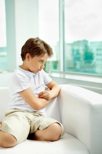 Mały chłopiec sulky, siedząc na kanapie — Zdjęcie stockowe