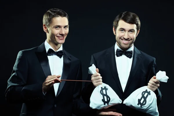 Les hommes en tuxedos tenant des sacs avec de l'argent — Photo