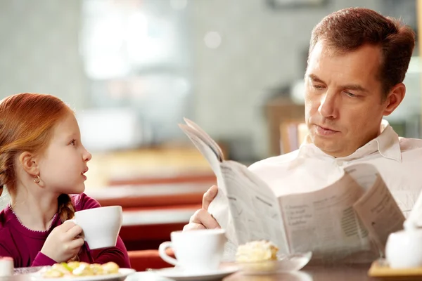 Ragazza parlando con suo padre assorbito nel giornale — Foto Stock