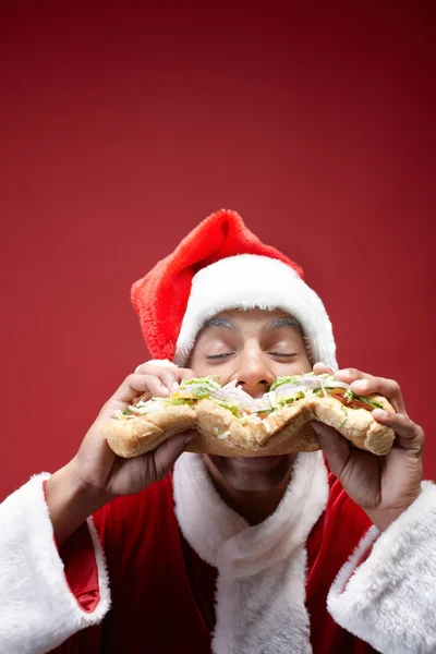 Papai Noel desfrutando delicioso sanduíche — Fotografia de Stock