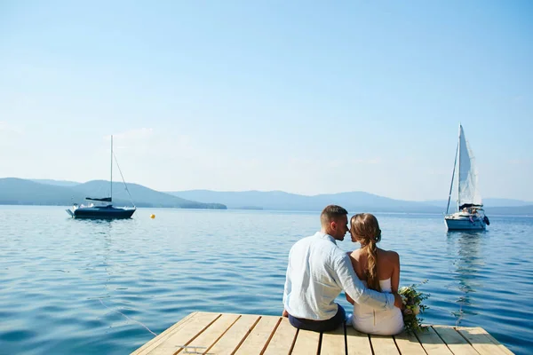 Románticos recién casados sentados junto al agua — Foto de Stock