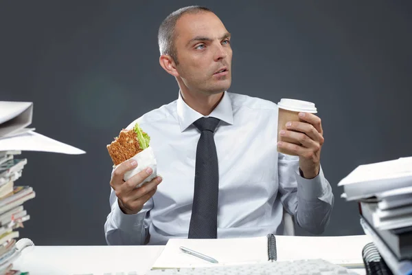 Gerente com sanduíche e café em seu local de trabalho — Fotografia de Stock