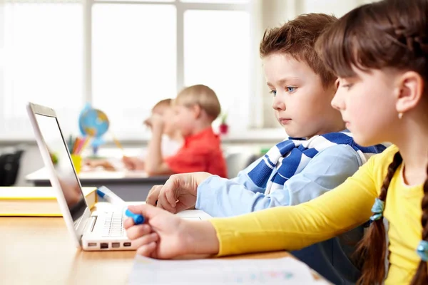 Children sitting at table and looking at laptop — Stock Photo, Image