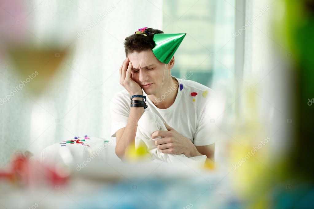 Man in party hat suffering from headache 