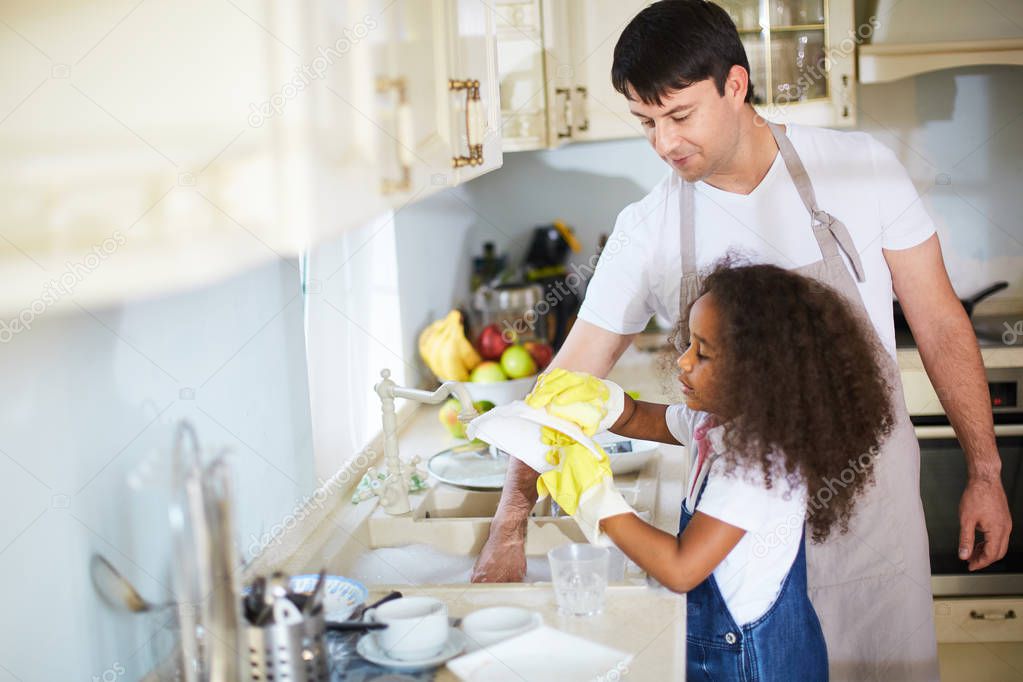 girl washing dishes with father