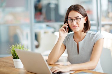 Dizüstü bilgisayarda çalışan ve telefonda konuşurken bir işkadını
