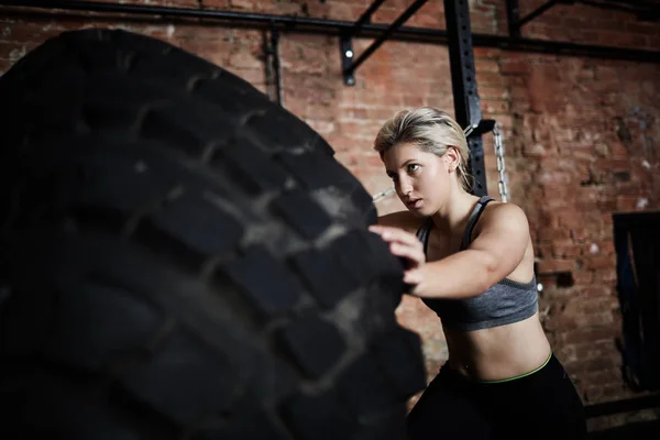 Atleta feminina virando pneu durante o treinamento — Fotografia de Stock