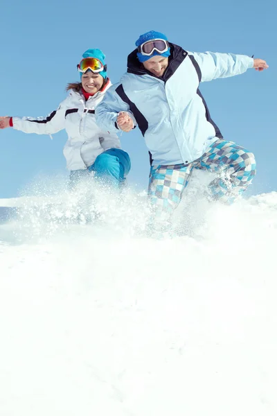 Glada par hoppning i snö — Stockfoto