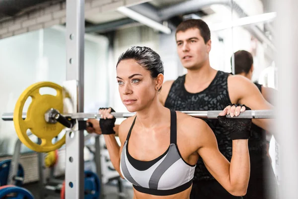 Mujer levantando peso en el gimnasio con su entrenador — Foto de Stock