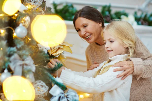 Vrouw en meisje opknoping speelgoed op kerstboom — Stockfoto