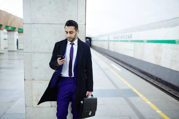 Чоловік стоїть на станції і використовує смартфон — стокове фото