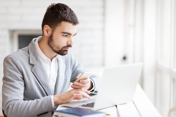 Business man using smartphone while working on laptop — стоковое фото