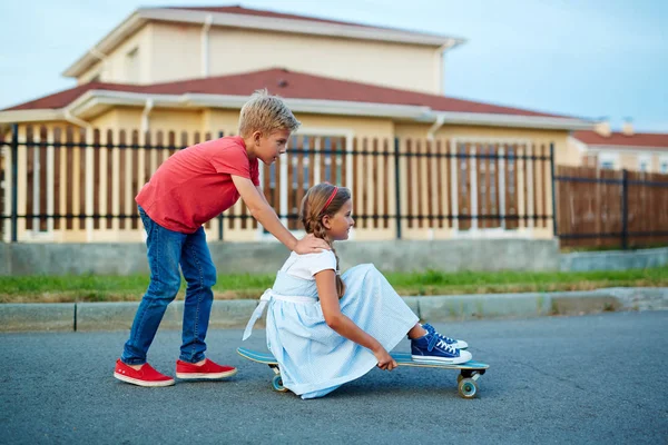 Αγόρι κάθεται στο skateboard πιέζει αδελφή — Φωτογραφία Αρχείου