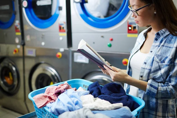Woman reading in laundrette — Stock Photo, Image