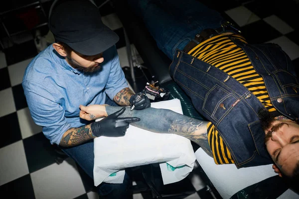 tattooer in ball-cap working with client